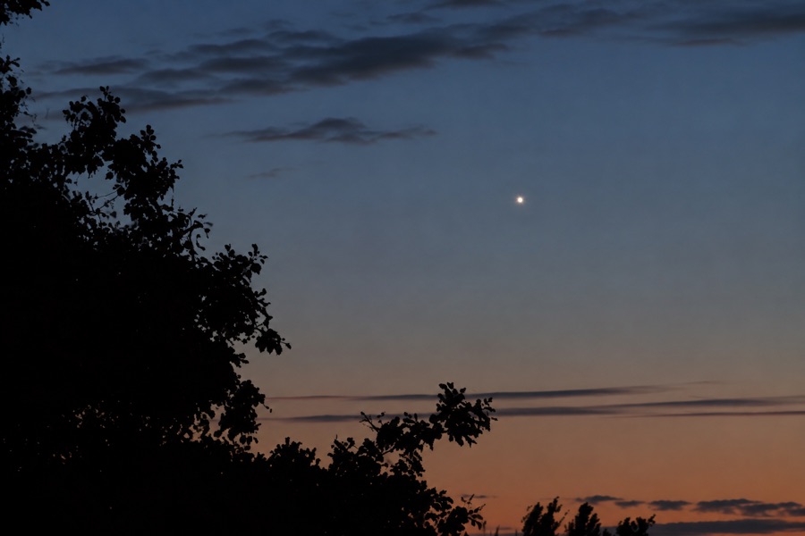 Venus shining as a bright point in the twilight sky above a dark horizon.